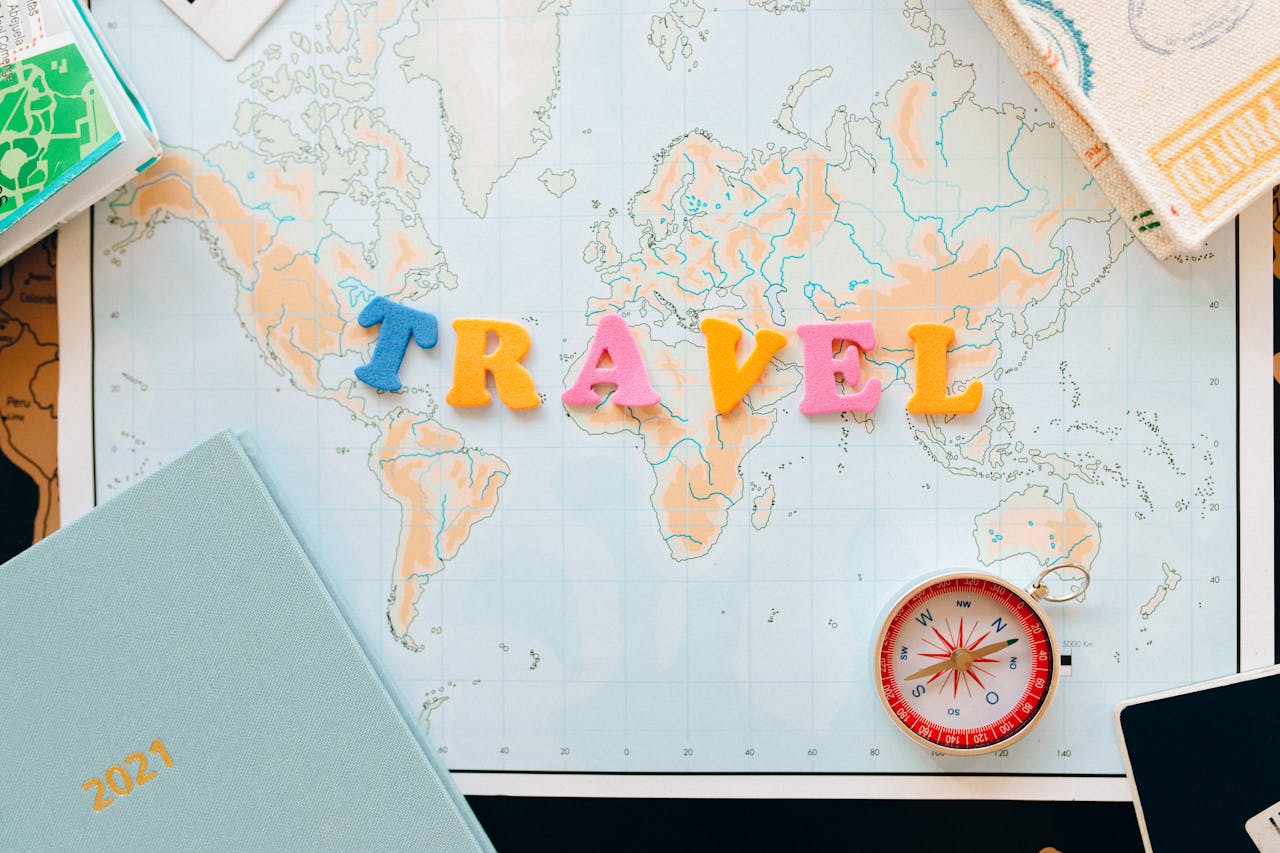 Flat lay of a map with colorful letters TRAVEL and a compass for planning adventures.